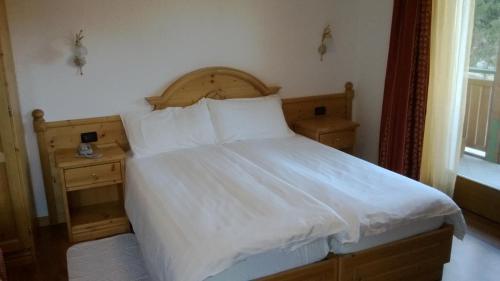 Una cama con sábanas blancas y almohadas en un dormitorio en Hotel Pineta, en Fiavè
