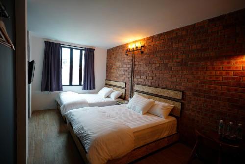two beds in a room with a brick wall at Brick Box Hotel @ Oldtown Ipoh in Ipoh