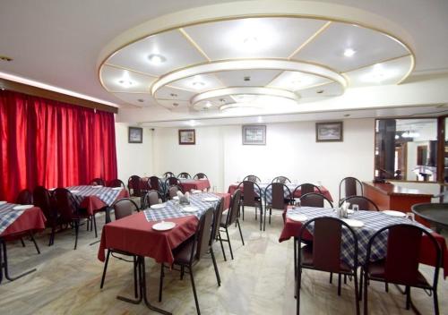 un comedor con mesas, sillas y cortinas rojas en Hotel Atul Regency Katra en Katra
