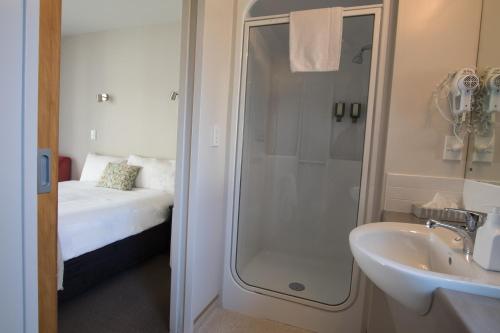 a bathroom with a shower and a sink and a bed at Bella Vista Motel Kaikoura in Kaikoura