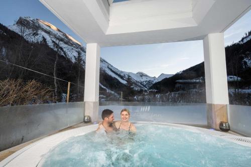 a man and woman in a hot tub with mountains at Adler Inn Tyrol Mountain Resort SUPERIOR in Tux