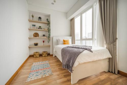 a white bedroom with a bed and a window at BUNGALOW by Kozystay 3BR Apartment at Kuningan in Jakarta