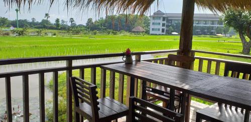 a wooden table and chairs on a balcony with a rice field at Oon Valley Farm Stay in Ban Mae Pha Haen