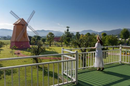 a woman in a white dress standing on a balcony with a windmill at Oon Valley Farm Stay in Ban Mae Pha Haen