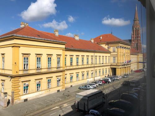 un grand bâtiment jaune avec des voitures garées dans un parking dans l'établissement Apartment Life Osijek, à Osijek