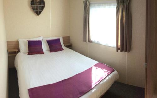 a bedroom with a bed with purple pillows and a window at Thurso Bay Holidays in Thurso