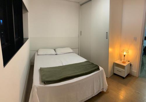 a small white bedroom with a bed and a lamp at 709- Apartamento Decorado Encantador, mobiliado, amplo, cozinha completa, Excelente localização no Rebouças in Curitiba