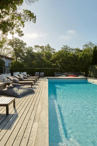 une piscine avec des chaises longues et une terrasse en bois dans l'établissement Hotel La Maison de la Prade, à Messanges
