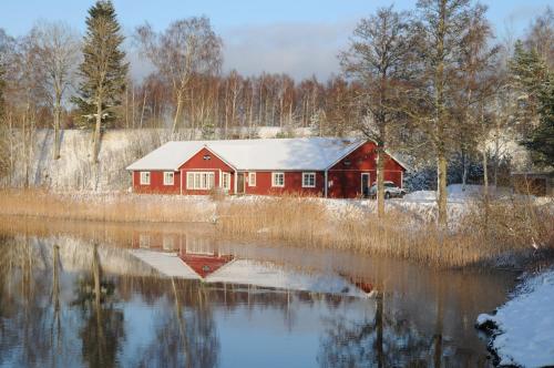 um celeiro vermelho com neve ao lado de um lago em Brovillan em Lekeryd
