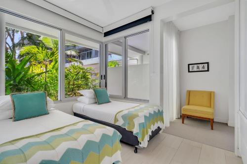 two beds in a room with windows and a chair at Elysium Private Apartments at The Drift Resort in Palm Cove