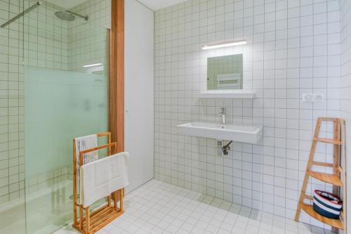 a white tiled bathroom with a sink and a shower at Les Terrasses de Piegu - vue mer et plage à 200 m in Pléneuf-Val-André