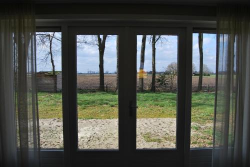 a view of a field through a glass door at Hoeve de Heemser Parel in Heemserveen