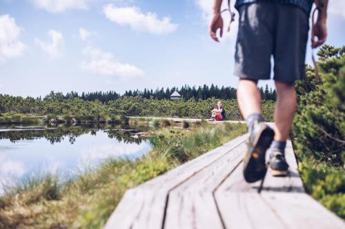 a person walking on a wooden path near a body of water at Pohorje Village Wellbeing Resort - Family Apartments Bolfenk in Pohorje
