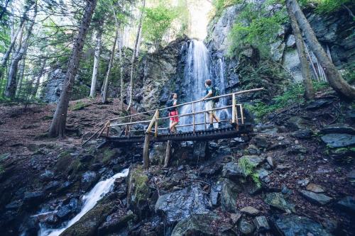 three people standing on a bridge in front of a waterfall at Pohorje Village Wellbeing Resort - Family Apartments Bolfenk in Pohorje