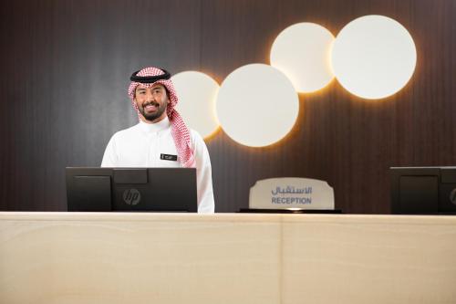 un hombre parado frente a un escritorio con un portátil en Qamar Hotel Jeddah en Yeda