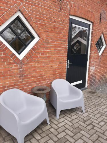 two white benches sitting in front of a brick building at Appartementen Hoek 1 in Baflo