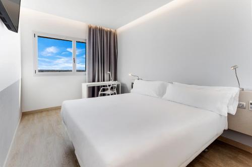 a white bedroom with a large bed and a window at B&B HOTEL Barcelona Viladecans in Viladecáns
