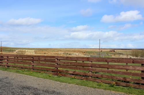 a wooden fence in a field with horses in the background at Hillside Camping Pods and Shepherd's Hut in Wick