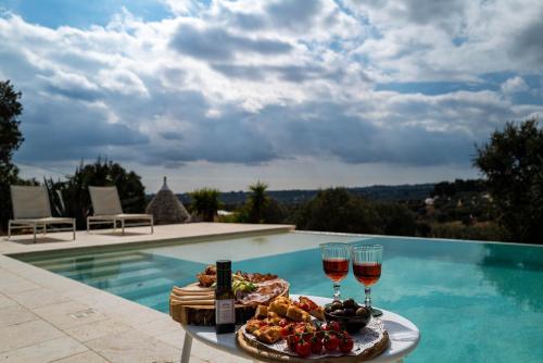 uma bandeja de comida e copos de vinho ao lado de uma piscina em Relais Trulli Le Icone em Ostuni