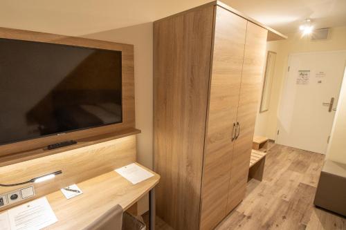 Habitación con TV grande y armario de madera. en Hotel Fallersleber Spieker, en Wolfsburg
