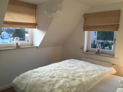 ein weißes Bett in einem Zimmer mit 2 Fenstern in der Unterkunft Lütje Deern in Hörnum