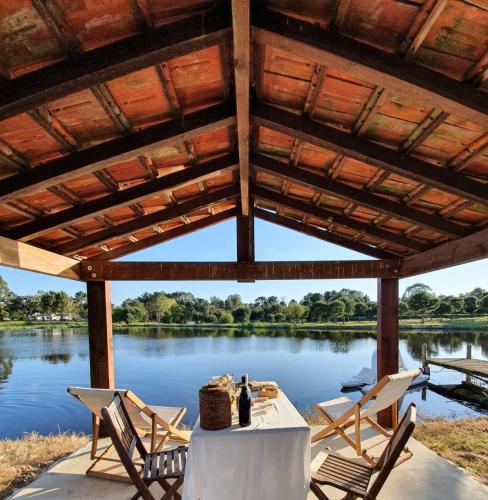 a table and chairs under a wooden pavilion with a lake at Casas da Horta in Alcácer do Sal