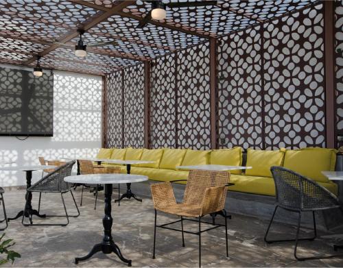 a room with a yellow couch and tables and chairs at The Xperience by g in Mazatlán