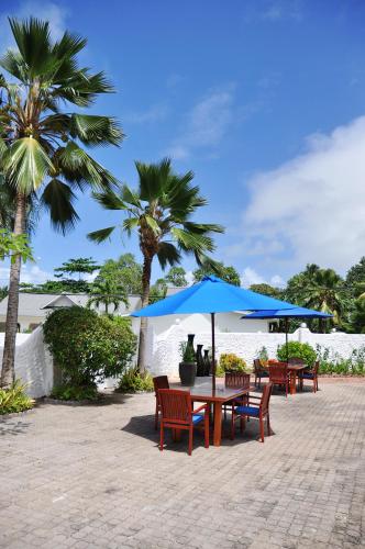 a table and chairs with a blue umbrella and palm trees at Britannia Hotel in Grand'Anse Praslin