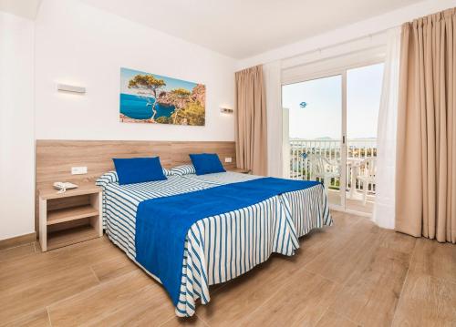 a bedroom with a blue and white bed and a window at Globales Condes de Alcudia in Port d'Alcudia