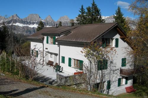 a white house with green shutters and mountains in the background at Casa Malanca, Flumserberg in Flums