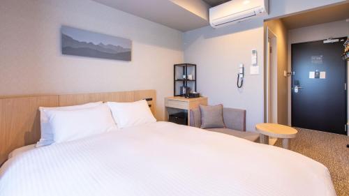 a bedroom with a large white bed and a chair at KOKO HOTEL Hidatakayama - formaly Hotel Wing Hida Takayama in Takayama