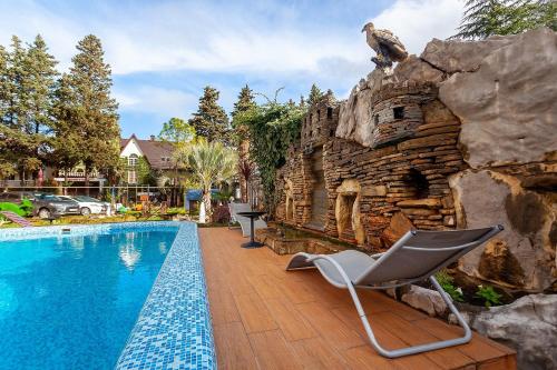 a swimming pool with a rock wall next to a house at Грейс Кристалл Отель in Adler