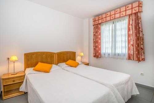 2 łóżka w sypialni z białą pościelą i pomarańczowymi poduszkami w obiekcie Apartamentos Hipocampos Unitursa w mieście Calpe