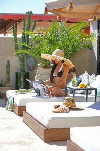 a woman in a straw hat sitting on a bed with a laptop at Dar Kandi in Marrakech
