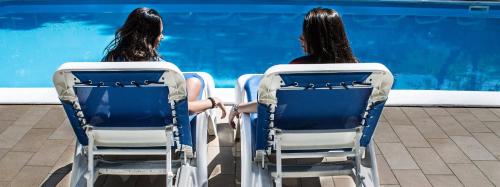 dos mujeres sentadas en sillas mirando a una piscina en Hotel Carillon, en Bellaria-Igea Marina