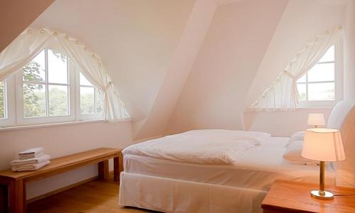 ein weißes Schlafzimmer mit einem Bett und zwei Fenstern in der Unterkunft Strandhaus hinter der Düne in Ahrenshoop