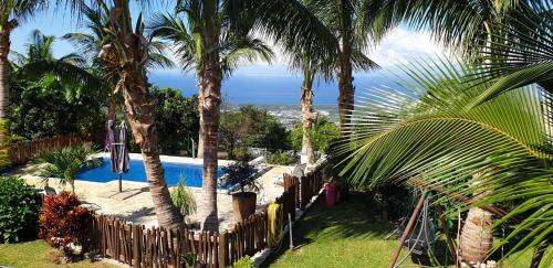 a swimming pool with palm trees and a fence at Au ti bonheur d'en O ' in Le Lambert