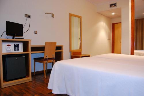 a bedroom with a bed and a desk with a television at Hotel Galaico in Sanxenxo