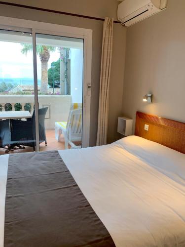 a bedroom with a bed and a desk and a balcony at Hôtel Beau Soleil in Le Lavandou