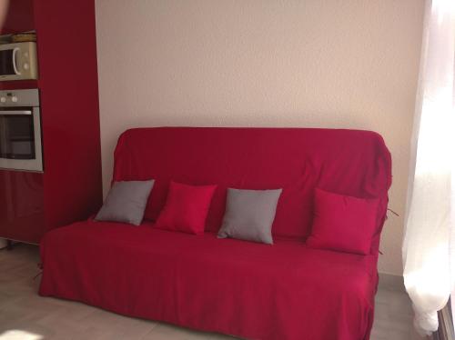 a red couch with four pillows in a room at Résidence le Neptuna 50 mètres plage réservation du samedi au samedi en haute saison in Cap d'Agde
