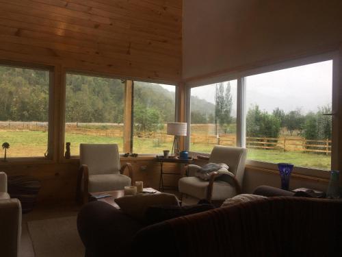 a living room with a couch and chairs and windows at Vuelta al Sur in Puelo