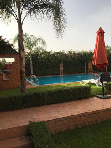 a swimming pool with a red umbrella and a woman in the background at Les Jardins de Ryad Bahia in Meknès