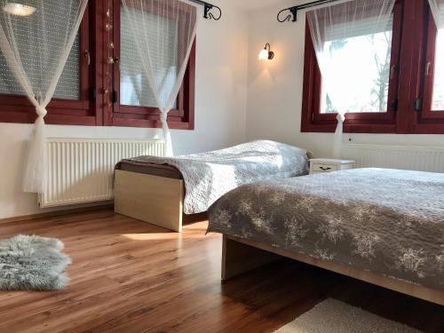 two beds in a bedroom with wooden floors and windows at Viharsarki Apartman in Gyula