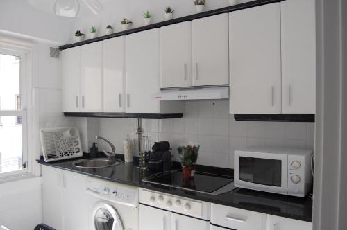 cocina blanca con microondas y fregadero en El Apartamento de Marta, en A Coruña