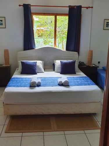 a bed with blue and white pillows and a window at La Digue Ylang Ylang in La Digue