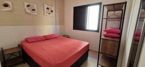 Un pequeño dormitorio con una cama roja y un estante en Apto aconchegante, bem localizado, churrasqueira na varanda, serviço de limpeza diária, serviço de praia - Pitangueiras - Guarujá, en Guarujá