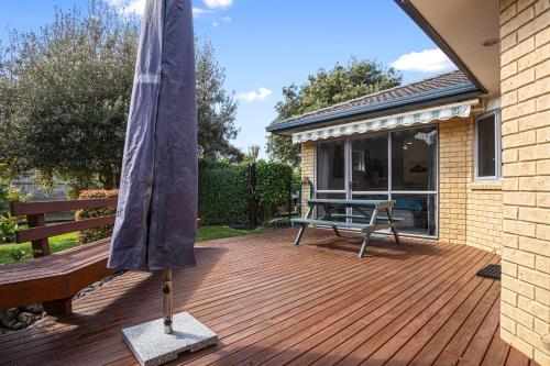 a wooden deck with a bench and an umbrella at Fantails Roost - Bowentown Holiday Home in Waihi Beach
