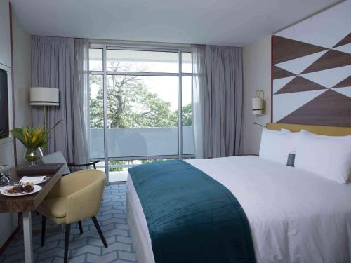 a hotel room with a bed and a desk and a window at Sofitel Abidjan Hotel Ivoire in Abidjan