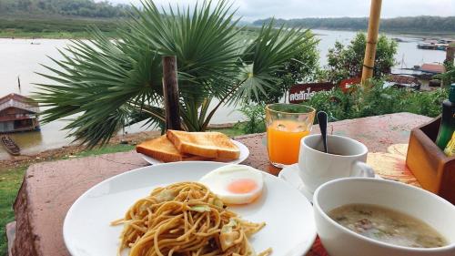 una mesa con un plato de espaguetis y huevos y una bebida en Baan Dongsak River view en Sangkhla Buri
