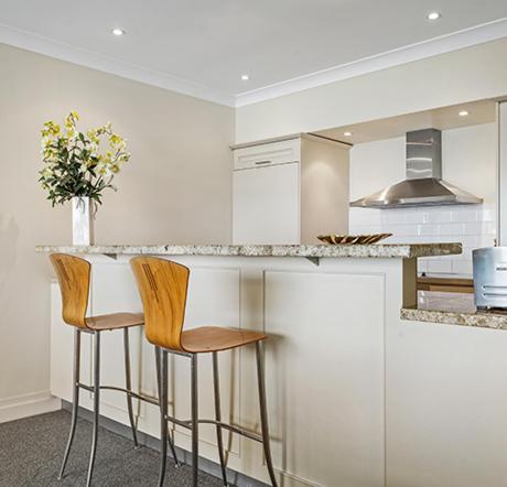 a kitchen with a counter and two stools at Auckland Waterfront Serviced Apartments on Prince's Wharf in Auckland